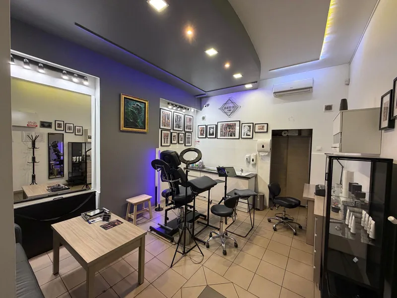 Wnętrze studia To Jest To Tattoo w Częstochowie: fotel do tatuowania, lampa pierścieniowa, ściana z oprawionymi pracami i logo studia, stanowisko pracy i część poczekalni